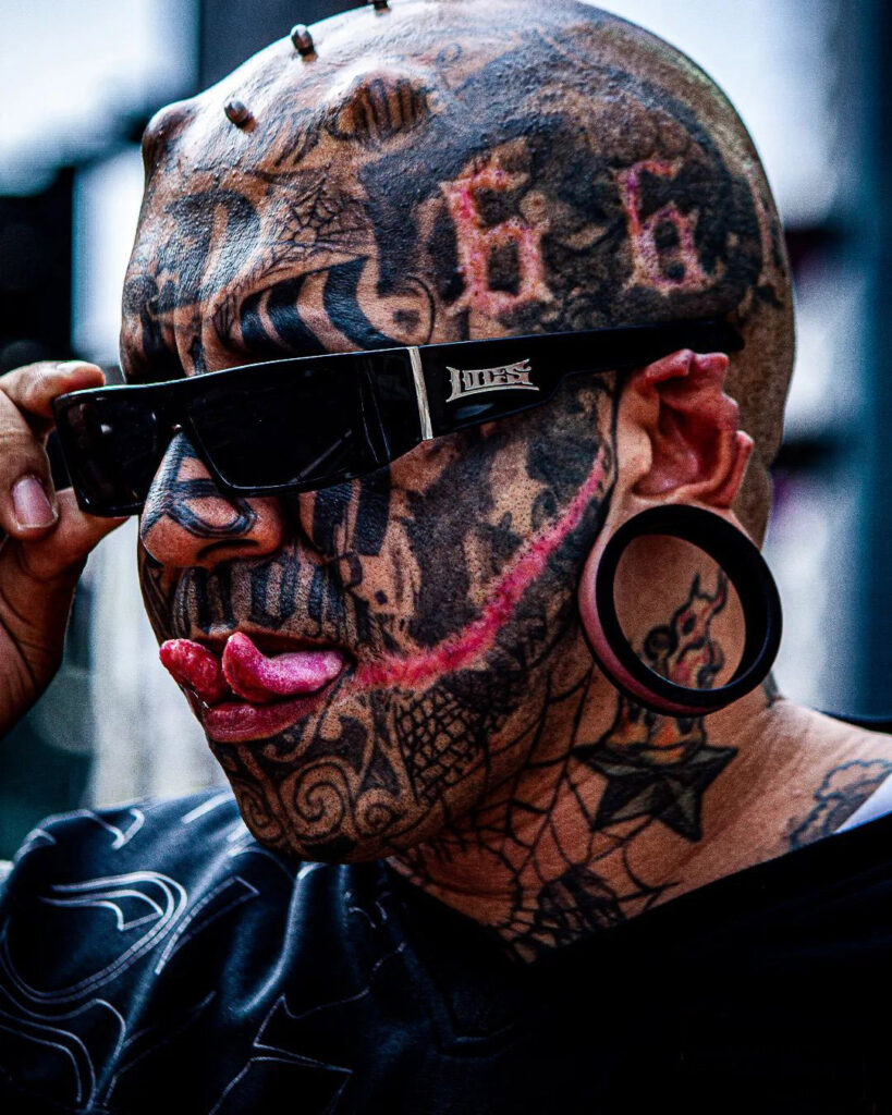 Renato sticks out his split tongue with his cropped ears and tattooed face.