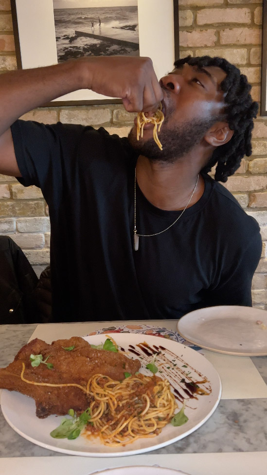 Emmanuel is shown with a plate full of spaghetti as he moves the stands into his mouth.